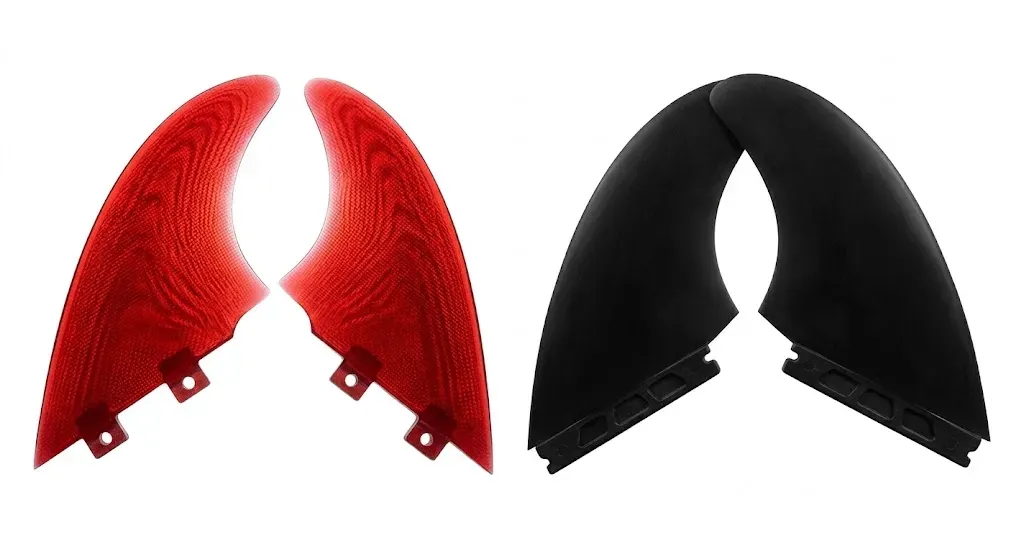 Side-by-side comparison of a translucent premium GFK surfboard fin and a black injection-molded plastic fin on a shaping rack.